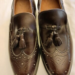 May include: A pair of dark brown leather loafers with decorative perforations and tassel accents. The shoes have a classic design, with a rounded toe and a low heel. The leather appears to be polished and in good condition.