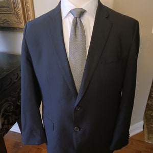 May include: A dark blue blazer with a gray patterned tie. The blazer has a single button closure and two pockets.