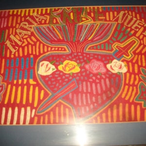 May include: A framed artwork depicting a red heart with a sword piercing through it. The heart is surrounded by roses and the words "MARIA JOSE" and "EVET" are written in gold lettering.