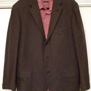 May include: A brown blazer with a red and white patterned shirt underneath. The blazer has a single button closure and two pockets on the front.