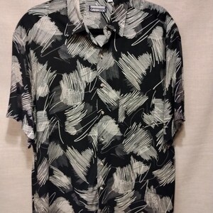 May include: Black button-down shirt with a white and grey scribble pattern. The shirt has short sleeves and a collared neckline. The brand name "OAKBROOK" is visible on the collar.