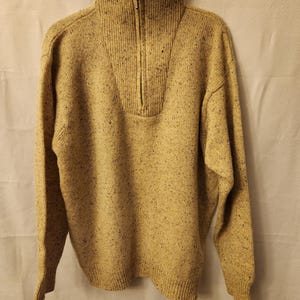 May include: A beige sweater with a half-zip closure and a speckled pattern.