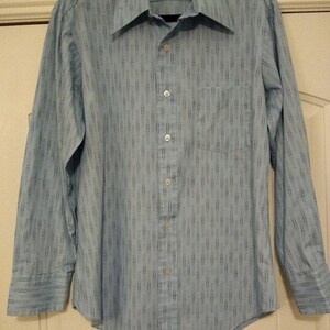 May include: A light blue long-sleeved button-down shirt with a subtle black and white patterned design.