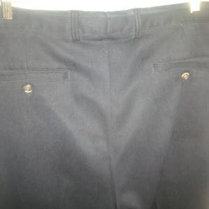 May include: A pair of dark gray dress pants with a subtle pinstripe pattern. The pants have two pockets on the back, each with a button closure.