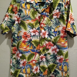 May include: A short-sleeved, button-up shirt with a tropical print featuring parrots, flowers, and palm leaves. The shirt has a white background with green, blue, red, yellow, and orange colors.