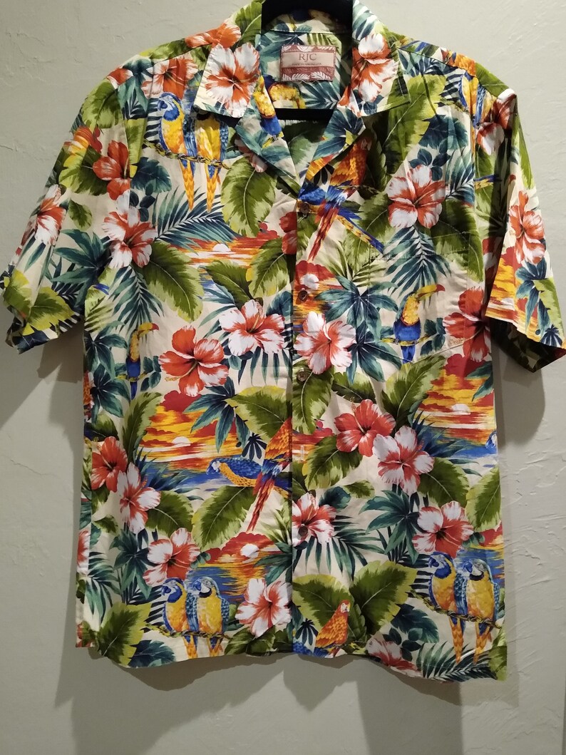 May include: A short-sleeved, button-up shirt with a tropical print featuring parrots, flowers, and palm leaves. The shirt has a white background with green, blue, red, yellow, and orange colors.