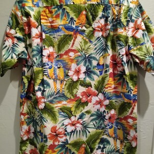 May include: A short-sleeved button-down shirt with a tropical print featuring parrots, flowers, and palm leaves in shades of green, blue, red, yellow, and orange.