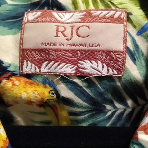 May include: A red and white label with the text "RJC" and "Made in Hawaii, USA". The label is attached to a white shirt with a tropical print.