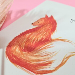 May include: A watercolor painting of a red fox curled up with its tail wrapped around its body. The fox is painted in shades of orange and yellow, with a white background.