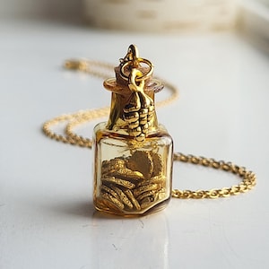 May include: Gold necklace featuring a small glass bottle pendant filled with gold coins and a gold grape charm.