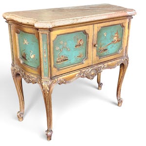 May include: A wooden cabinet with a light marble top and curved legs. The front features two doors painted in a teal green hue, decorated with gold-toned illustrations of birds, trees, and structures. The frame has carved details.