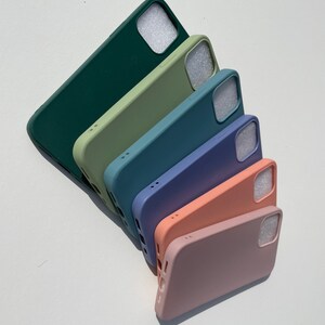 Puede incluir: Un conjunto de seis fundas de silicona para smartphone dispuestas en fila diagonal, con un degradado de color desde verde bosque oscuro a verde salvia claro, azul cerceta, azul bígaro, melocotón y rosa empolvado, con recorte cuadrado.