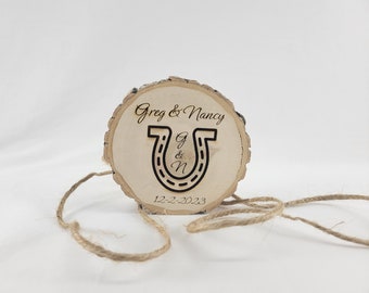 May include: A wooden ring bearer box with a horseshoe design and the text "Greg & Nancy" and "12-2-2023".