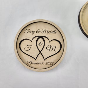 May include: A wooden ring bearer box with a carved design of two intertwined hearts with the initials "T" and "M" inside. The box is inscribed with the text "Terry & Michelle" and "November 7, 2022".