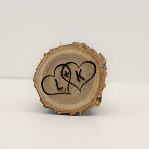 May include: A wooden slice with two intertwined hearts, each with a letter inside. The hearts are carved into the wood and the letters are "L" and "K".