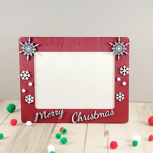 May include: Red wooden picture frame with white snowflakes and the words "Merry Christmas" on the bottom.