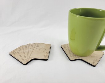 May include: A set of six wooden coasters featuring a royal flush of hearts playing cards. The coasters are made of light brown wood and have a black border. A green mug is sitting on one of the coasters.