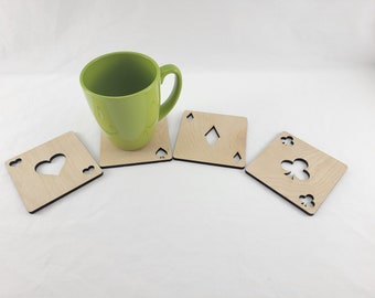 May include: Four wooden coasters with a different card suit cut out of each. The coasters are light brown and have a dark brown border. A green mug is sitting on one of the coasters.