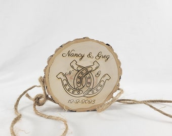 May include: A wooden slice with the text "Nancy & Greg" and two intertwined horseshoes. The date "12-2-2023" is also engraved on the slice.