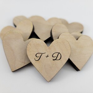 May include: A pile of small, light brown wooden hearts with the initials "T + D" engraved on one of the hearts.
