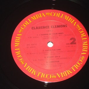 Pu&ograve; includere: Un disco in vinile vintage di Clarence Clemons, intitolato "Hero". L'etichetta rossa presenta il logo Columbia Records e titoli di canzoni come "I Wanna Be Your Hero" e "Kissin' On U". Il disco &egrave; nero con un'etichetta rossa.