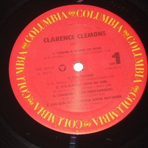 Pu&ograve; includere: Un disco in vinile vintage di Clarence Clemons, intitolato "Hero". L'etichetta rossa presenta il logo Columbia e titoli di canzoni come "You're a Friend of Mine" e "Liberation Fire". Il disco &egrave; nero con un'etichetta rossa.