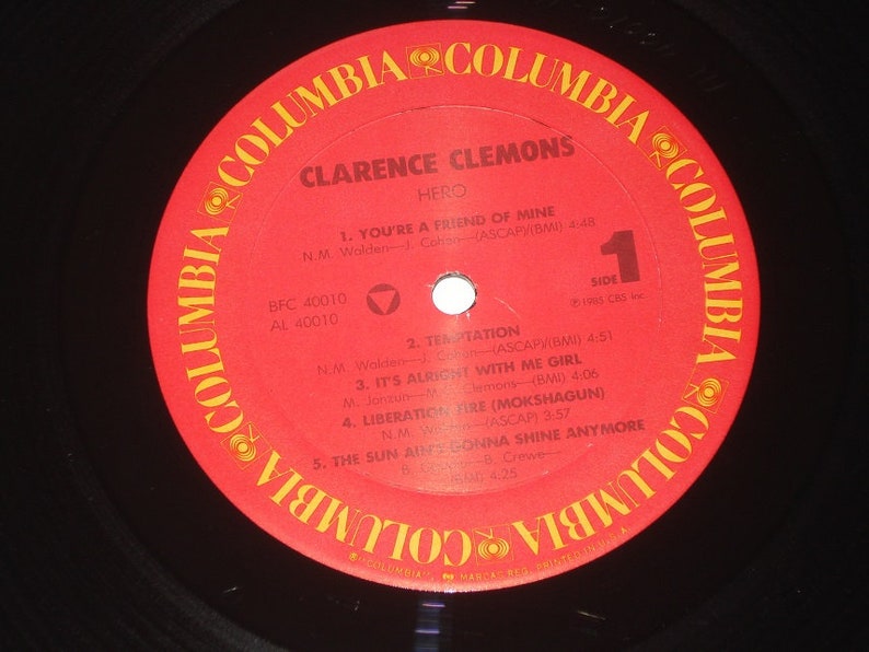Pu&ograve; includere: Un disco in vinile vintage di Clarence Clemons, intitolato "Hero". L'etichetta rossa presenta il logo Columbia e titoli di canzoni come "You're a Friend of Mine" e "Liberation Fire". Il disco &egrave; nero con un'etichetta rossa.