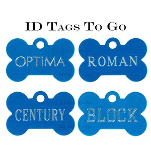 Puede incluir: Cuatro etiquetas de identificaci&oacute;n para perros de hueso azul con letras plateadas. Las etiquetas dicen "OPTIMA", "ROMAN", "CENTURY" y "BLOCK".