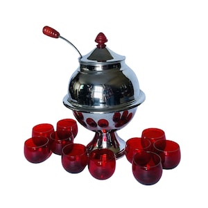 May include: A silver punch bowl with a red knob on the lid and a red wooden handle. The bowl is surrounded by 10 red glass cups.