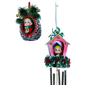 May include: Two vintage Christmas ornaments featuring a whimsical elf figure. The first ornament is a pine cone with a small elf peeking out from a window. The second ornament is a pink birdhouse with a larger elf figure inside. Both ornaments have a green garland and bells.