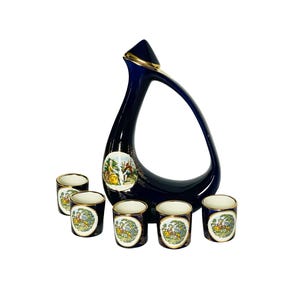 May include: A cobalt blue ceramic decanter with a gold trim and a set of six matching shot glasses. Each glass features a colorful painted scene of people in a garden.