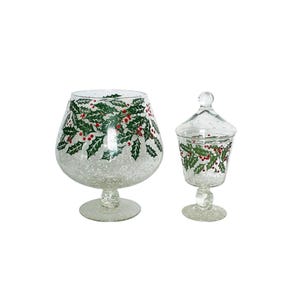 May include: Two clear glass decorative pieces. One is a large, stemmed bowl, and the other is a smaller, lidded candy dish. Both are decorated with a pattern of green holly leaves and red berries, perfect for holiday decor.