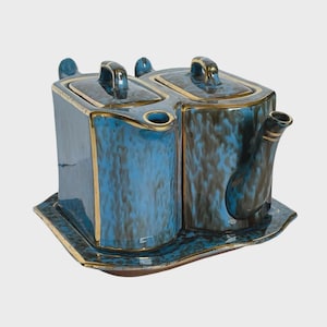 May include: A set of two rectangular ceramic teapots with lids, featuring a mottled blue and brown glaze with gold-toned trim. The teapots are positioned side-by-side on a matching rectangular ceramic tray with a wavy edge and gold trim.