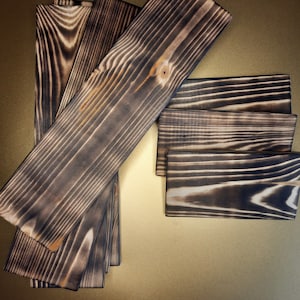 May include: A set of six wooden boards with a dark brown, charred finish. The boards are arranged in a fan shape, with the largest board at the top and the smallest board at the bottom.