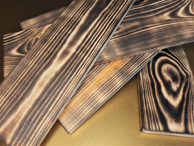 May include: Four pieces of dark brown wood planks with a charred finish. The wood grain is visible and the planks are stacked on top of each other.