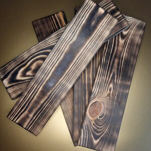 May include: Four pieces of dark wood with a charred finish. The wood has a natural grain pattern and a knot in one of the pieces.
