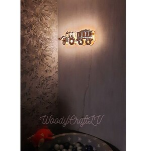 May include: A wooden tractor and trailer night light with a warm glow. The tractor is brown and the trailer is black. The light is mounted on a wall.