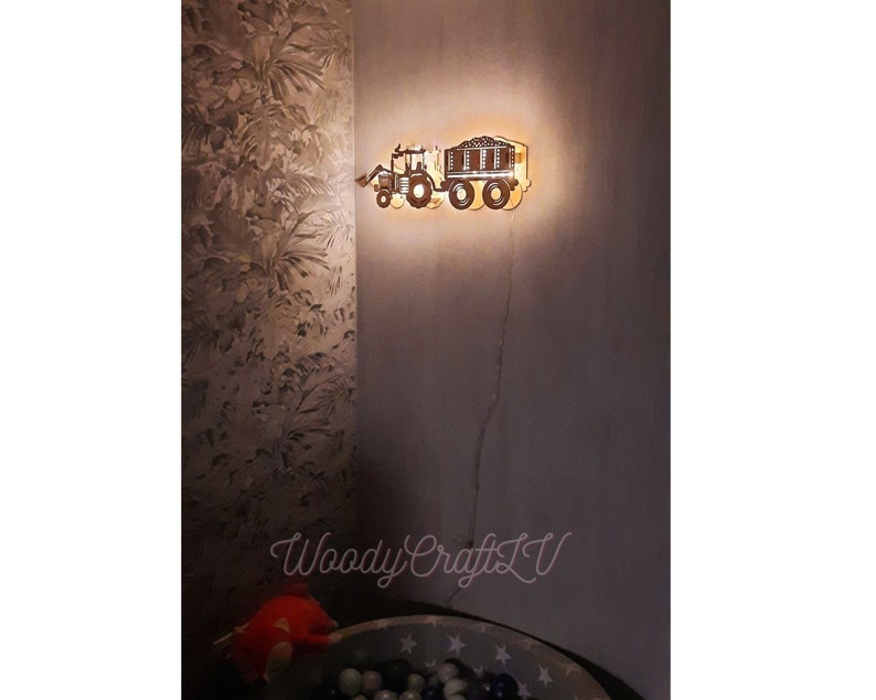 May include: A wooden tractor and trailer night light with a warm glow. The tractor is brown and the trailer is black. The light is mounted on a wall.