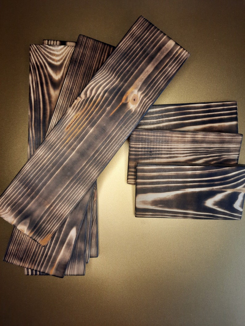 May include: A set of six wooden boards with a dark brown, charred finish. The boards are arranged in a fan shape, with the largest board at the top and the smallest board at the bottom.