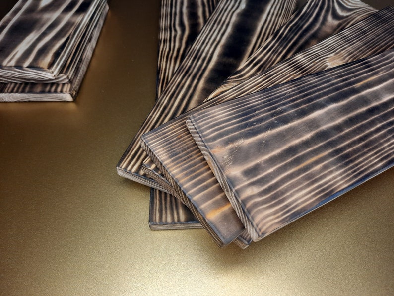 May include: Close-up of several wooden planks with a dark, charred finish. The planks have a natural wood grain pattern and are arranged in a fan shape.