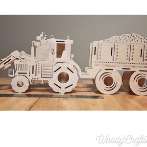May include: A wooden model of a tractor with a trailer. The tractor has a scoop on the front and the trailer has a bed filled with dirt. The model is made of unfinished wood.