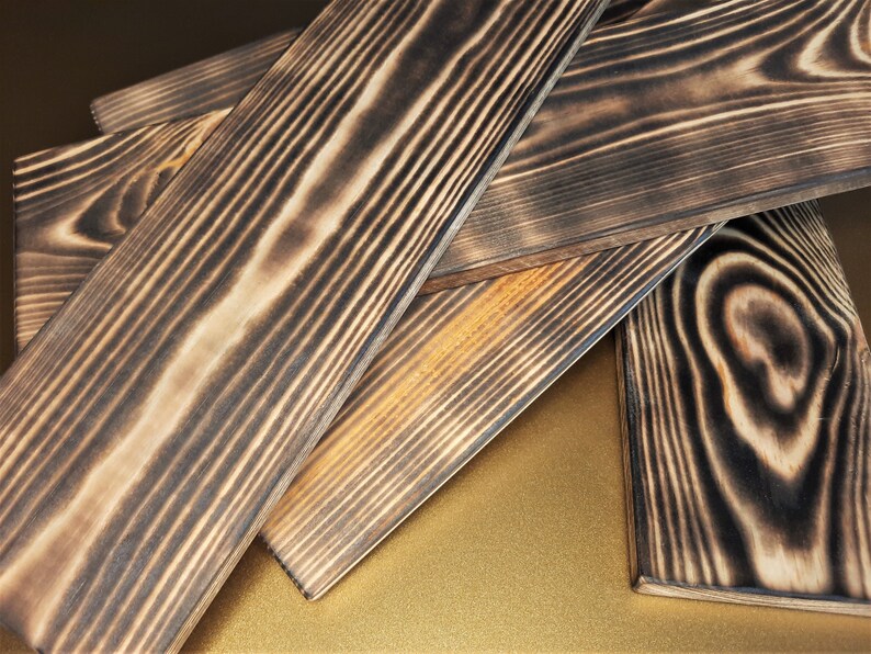 May include: Four pieces of dark brown wood planks with a charred finish. The wood grain is visible and the planks are stacked on top of each other.