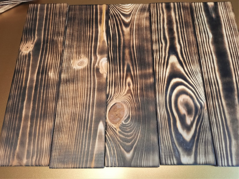 May include: Four wooden planks with a dark brown, burnt wood finish. The planks have a natural wood grain pattern and are arranged side by side.