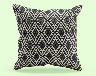May include: Square cushion with a geometric diamond pattern in black, cream, and olive green. The cushion has a soft, textured appearance, suitable for home decor. The design features repeating diamond shapes.