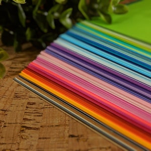 May include: A vibrant array of colorful paper sheets, fanned out to display a spectrum of hues. The colors range from warm reds and oranges to cool blues and greens, creating a visually appealing gradient. The paper is neatly stacked, suggesting a craft or stationery product.