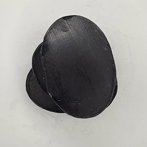 May include: A stack of three solid black oval-shaped bars with a smooth, slightly textured surface. Each bar features a consistent dark charcoal colour and a rounded edge profile, arranged in a slightly offset vertical pile against a plain background.