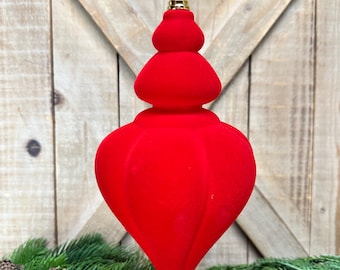 May include: A bright red, teardrop-shaped finial ornament with a smooth, velvet-like texture. The ornament features a tiered, bulbous top section and a pointed base, topped with a metallic gold cap and a thin gold hanging string for display.
