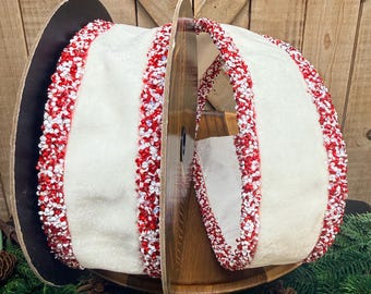 Può includere: Una bobina di nastro in tessuto largo color bianco sporco con bordi decorativi rivestiti di piccole perline testurizzate rosse e bianche. Il nastro è avvolto attorno a un nucleo di cartone circolare scuro, mostrando un motivo continuo.