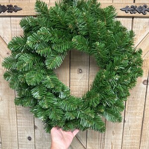 May include: A green artificial Christmas wreath with a natural pine look, hanging on a wooden door.