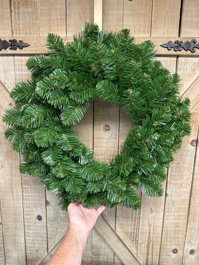 May include: A green artificial Christmas wreath with a natural pine look, hanging on a wooden door.